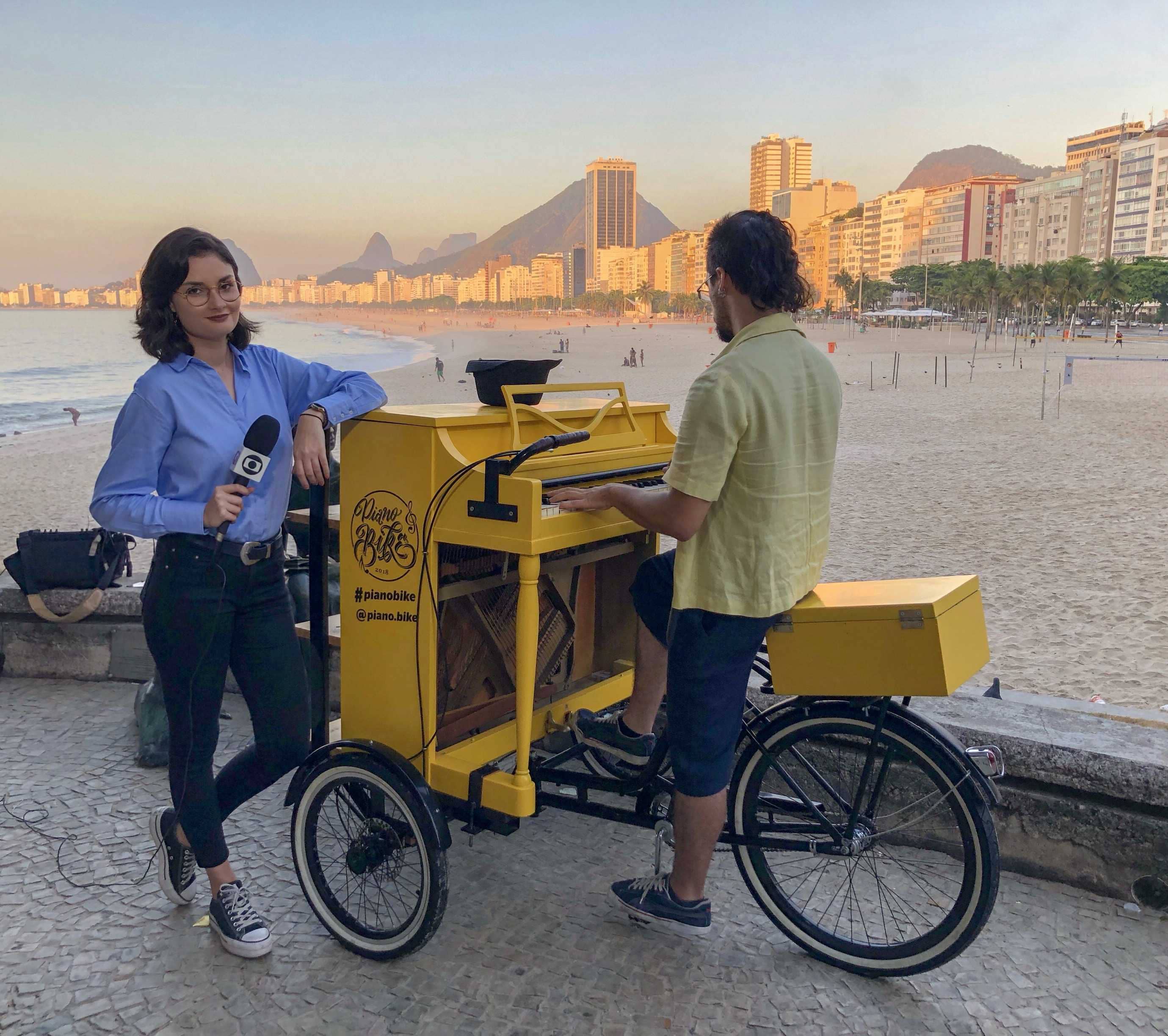 Foto do autor da página em um piano montado em uma bicicleta em uma entrevista com a Rede Globo